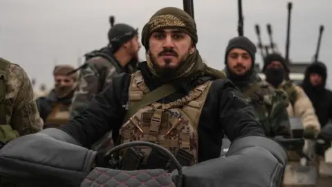 EPA Syrian troops stand together as one soldier sits on a motorcycle, wearing tactical gear and surrounded by others carrying weapons.
