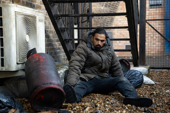 543570,TITLE:Eastenders Ravi sits clumsily among some leaves in a wasteland in EastEnders