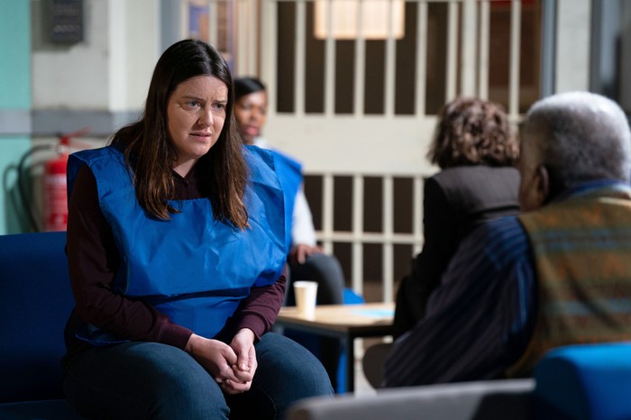 Zoe, in a blue bib, chats to Patrick in the prison visiting room in a scene from EastEnders