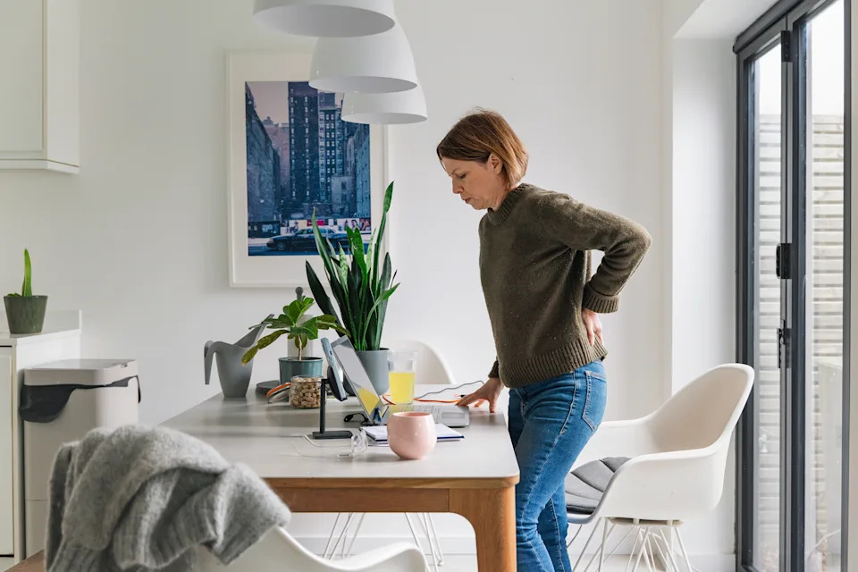 A mature woman (in her 40s) stands up whilst working from home. Her back twinges and she winces in pain. Poor posture/seating?