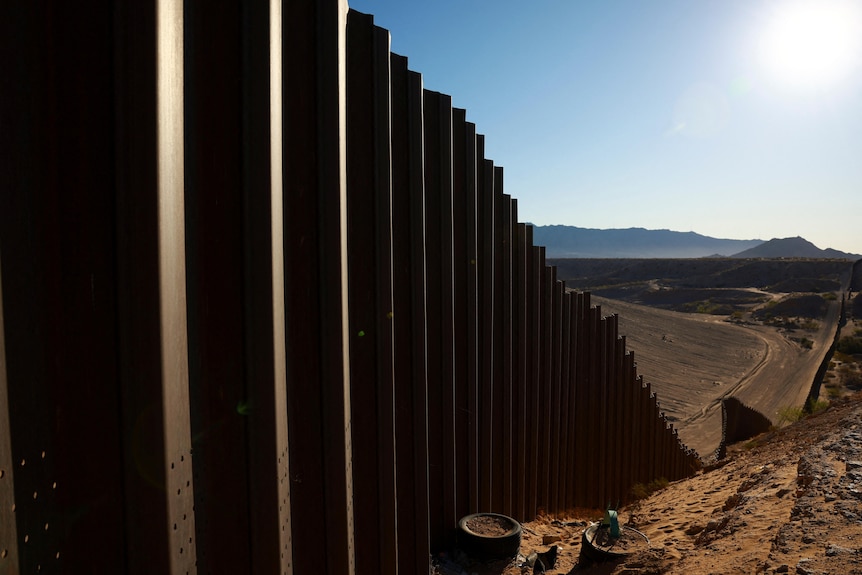 Metal pillars lined up to form a lengthy wall across arid land