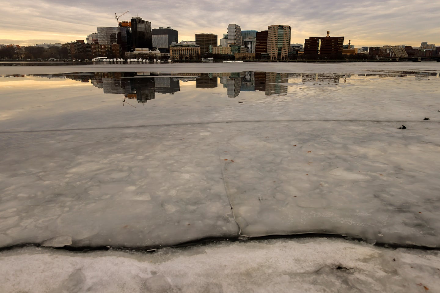 Buildings in Kendall Square in Cambridge are reflected on Charles River ice and water as seen from the Esplanade on January 14, 2026.
