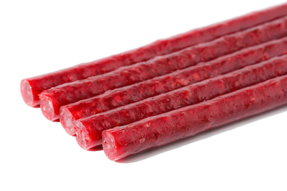 Five sticks of red licorice candy are arranged on a white background