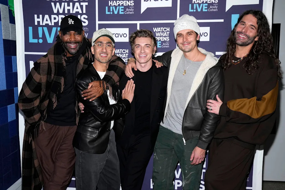 Karamo Brown, Tan France, Jeremiah Brent, Antoni Porowski, and Jonathan Van Ness smiling and posing together in casual and trendy outfits at a media event with a Watch What Happens Live backdrop