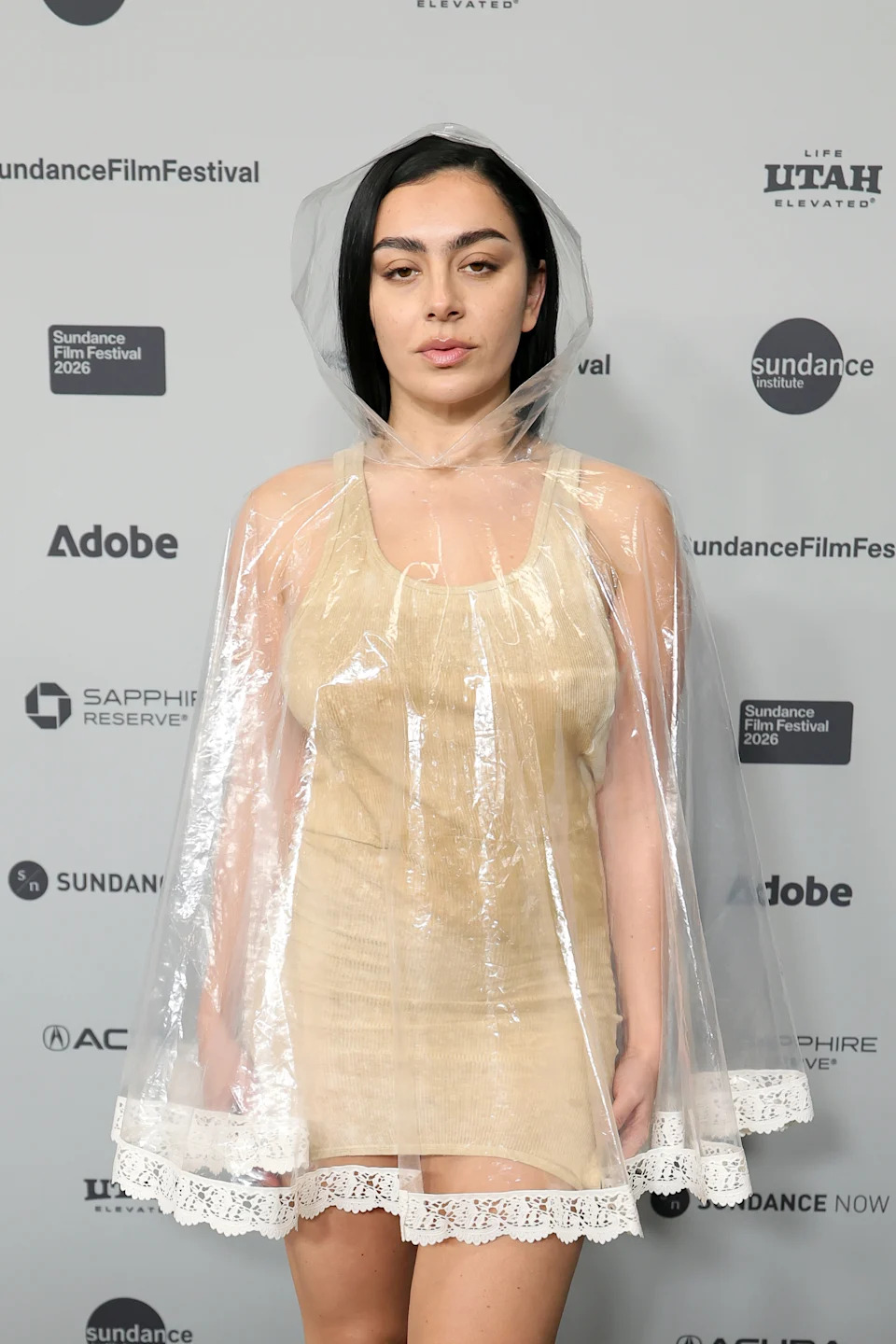Charli XCX in a Simon Carle spring 2024 look attends "The Gallerist" Premiere during the 2026 Sundance Film Festival. Charli XCX style, sundance style, clear poncho, hooded red carpet looks