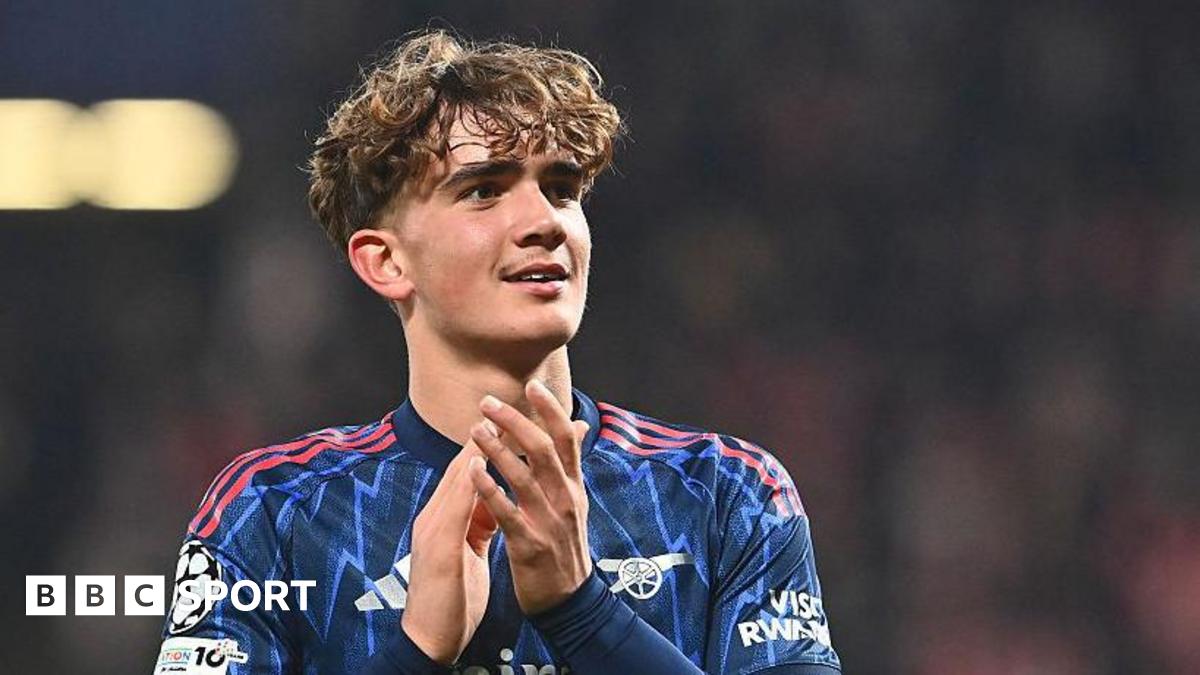Arsenal midfielder Max Dowman applauds as he celebrates the team's victory in the Champions League match against Slavia Prague. He is wearing a blue patterned Arsenal shirt, with three red stripes as trim.