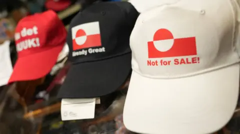 Reuters Caps with slogans supporting Greenland placed on a shelf. The slogans on the caps include "Not for SALE!" and "Already Great".