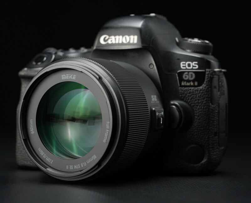A close-up of a Canon EOS 6D Mark II DSLR camera with a Meike 85mm f/1.8 lens, displayed on a dark surface with a black background.