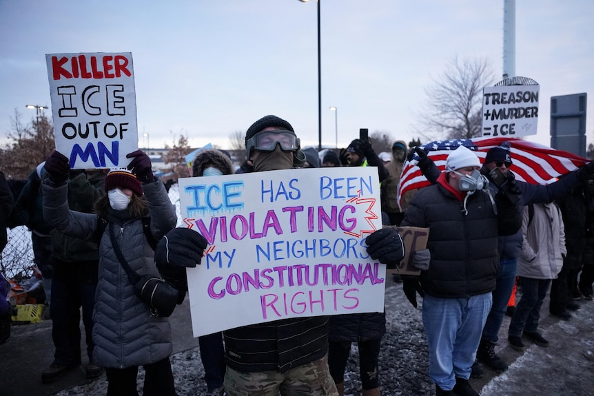 Two federal officers in military-grade gear arresting a protester.