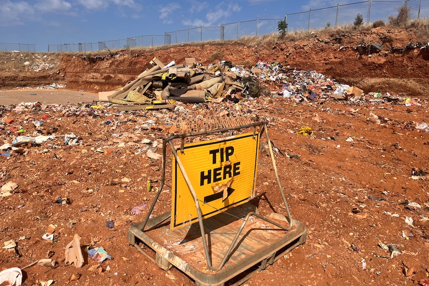 A yellow 'tip here' sign with an arrow at a rubbish dump.