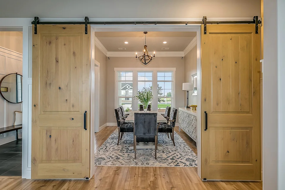 Open sliding barn doors reveal a dining room with a table, chairs, chandelier, and a large window overlooking the outside