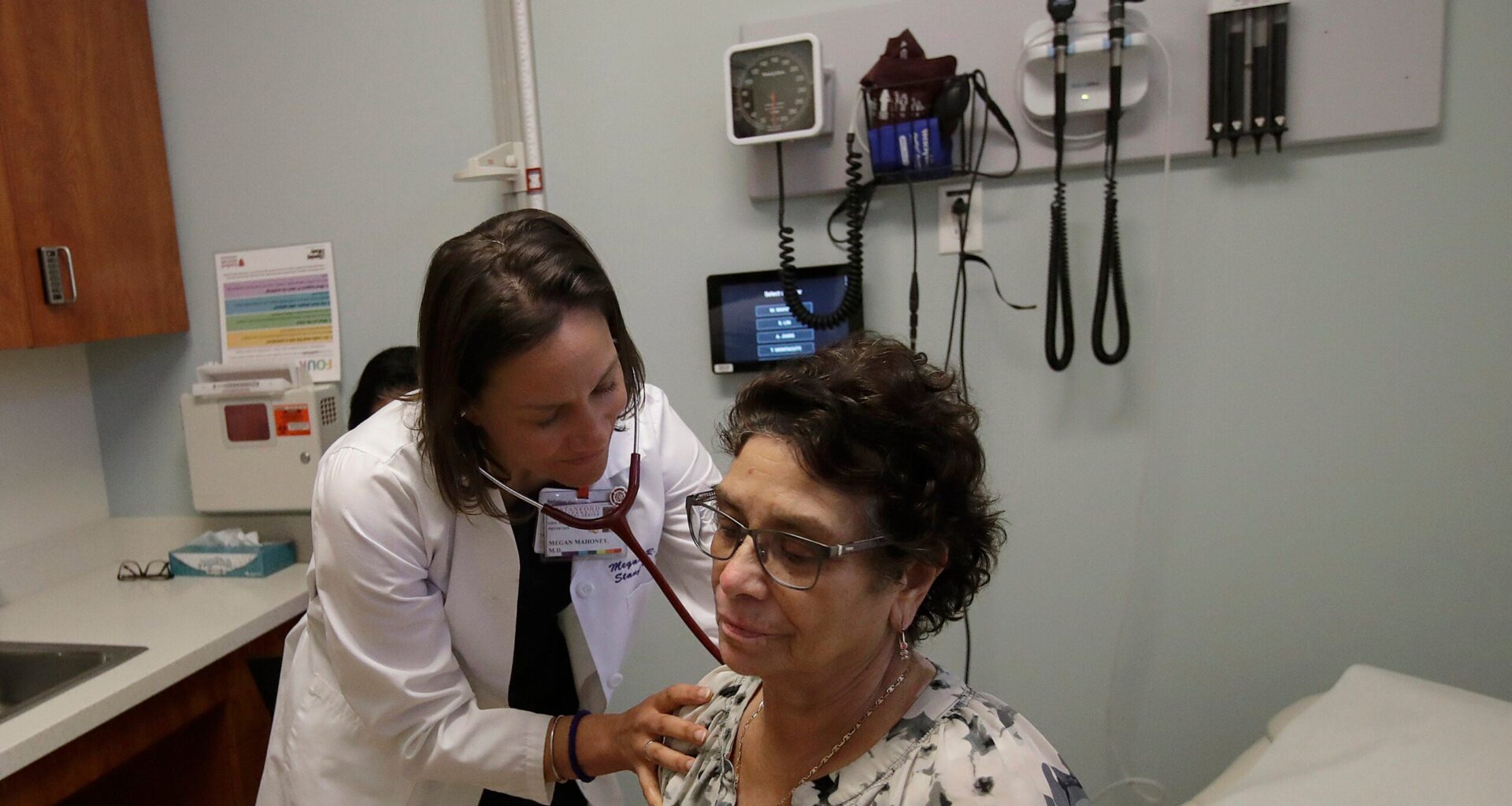 A doctor uses a stethoscope to listen to a patients back during a medical examination in a clinic room.