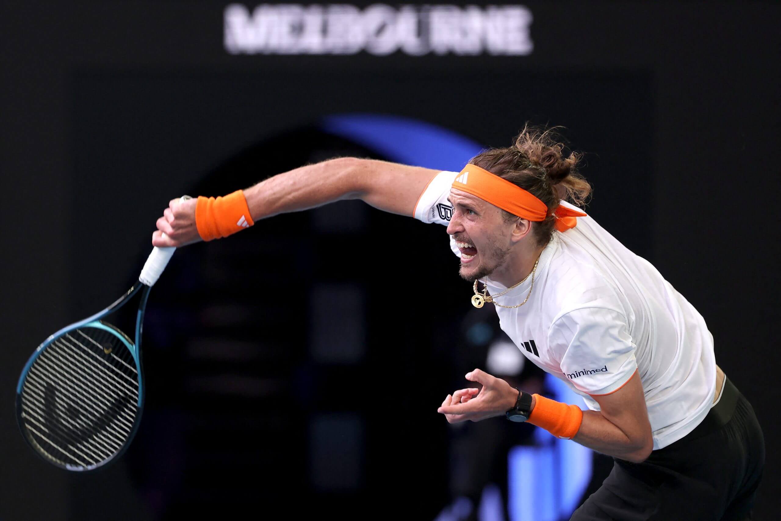 Alexander Zverev hits a serve and exhales, wearing a white tennis outfit and orange accents.