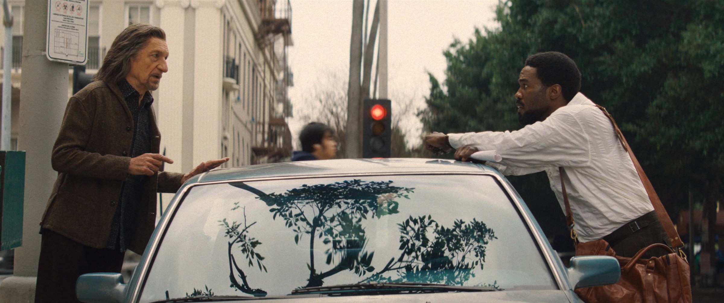 Two men looking at one another over the hood of a car.