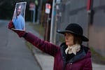 Karen James holds up a photograph of Alex Pretti, a VA nurse and U.S. citizen who was killed by two U.S. Customs and Border Protection agents in Minneapolis on Jan. 24, 2026, as immigration officers drive out of the U.S. Immigration and Customs Enforcement facility in Portland, Ore., on Jan. 27, 2026. A couple dozen gathered outside the facility following a vigil, which James attended, outside the Portland Veterans Affairs Medical Center in remembrance of Pretti.