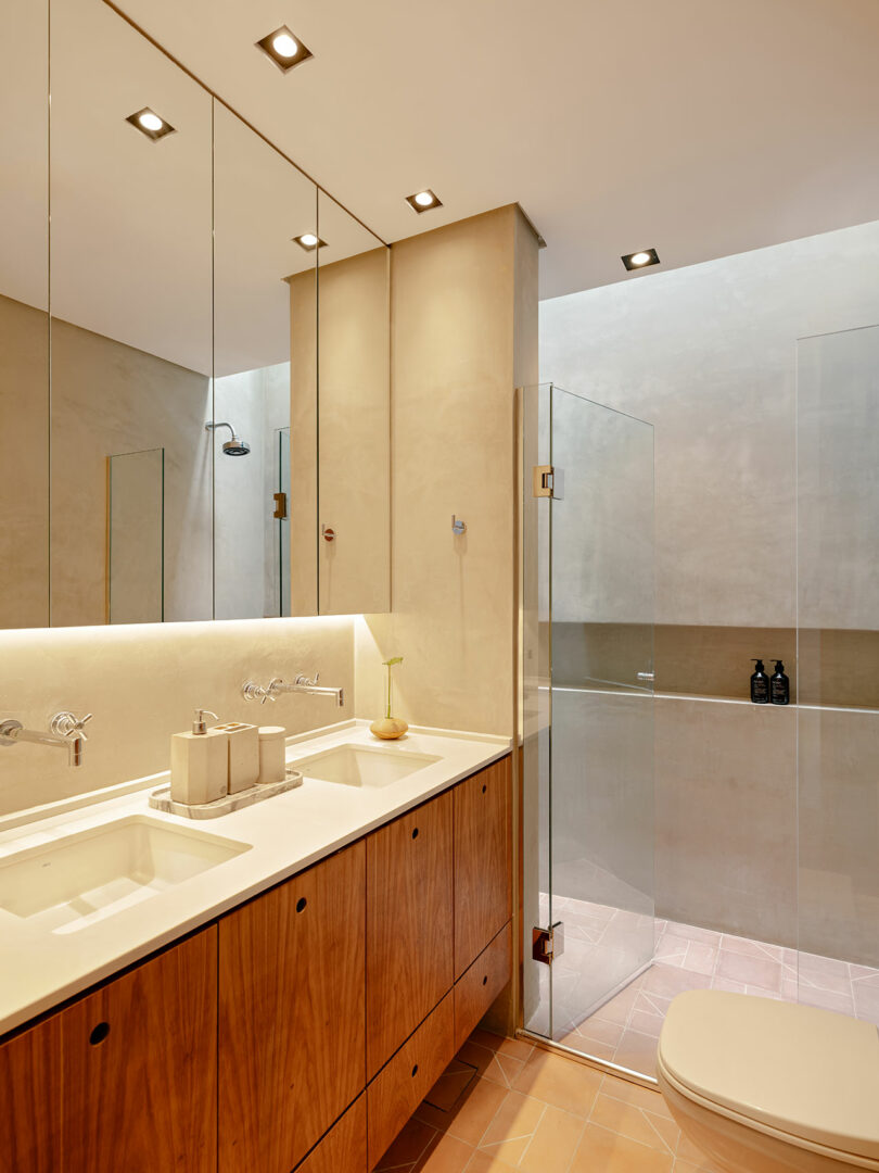 Modern bathroom with a double sink vanity, wooden cabinets, large mirrors, glass shower enclosure, and recessed ceiling lights.