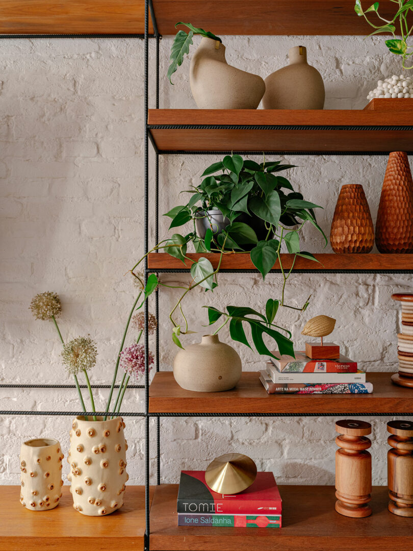 Wooden shelves with ceramic vases, green plant, books, wooden objects, and decorative items against a white brick wall.