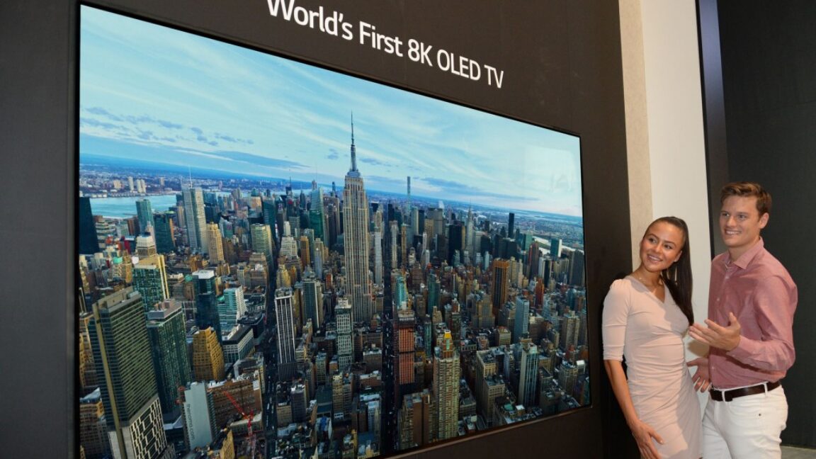 A man and woman standing next to a TV labeled the "world's first 8K OLED TV."