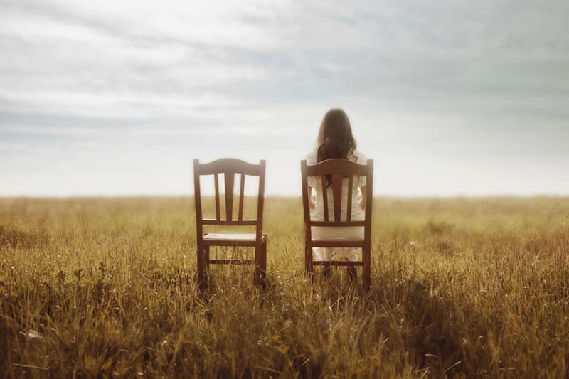 A solitary figure sits between two empty wooden chairs in a wide, open field, symbolizing faith, reflection, and the quiet global reach of Meridian Magazine and Latter-day Saint readers around the world.