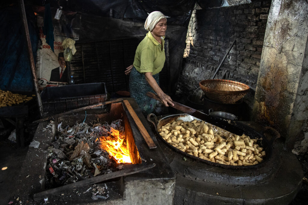 A worker fries tofu over a furnace fueled by a combination of plastic waste, wood and coconut husks at a tofu factory on May 22, 2025, in Sidoarjo, Indonesia. Credit: Robertus Pudyanto/Getty Images