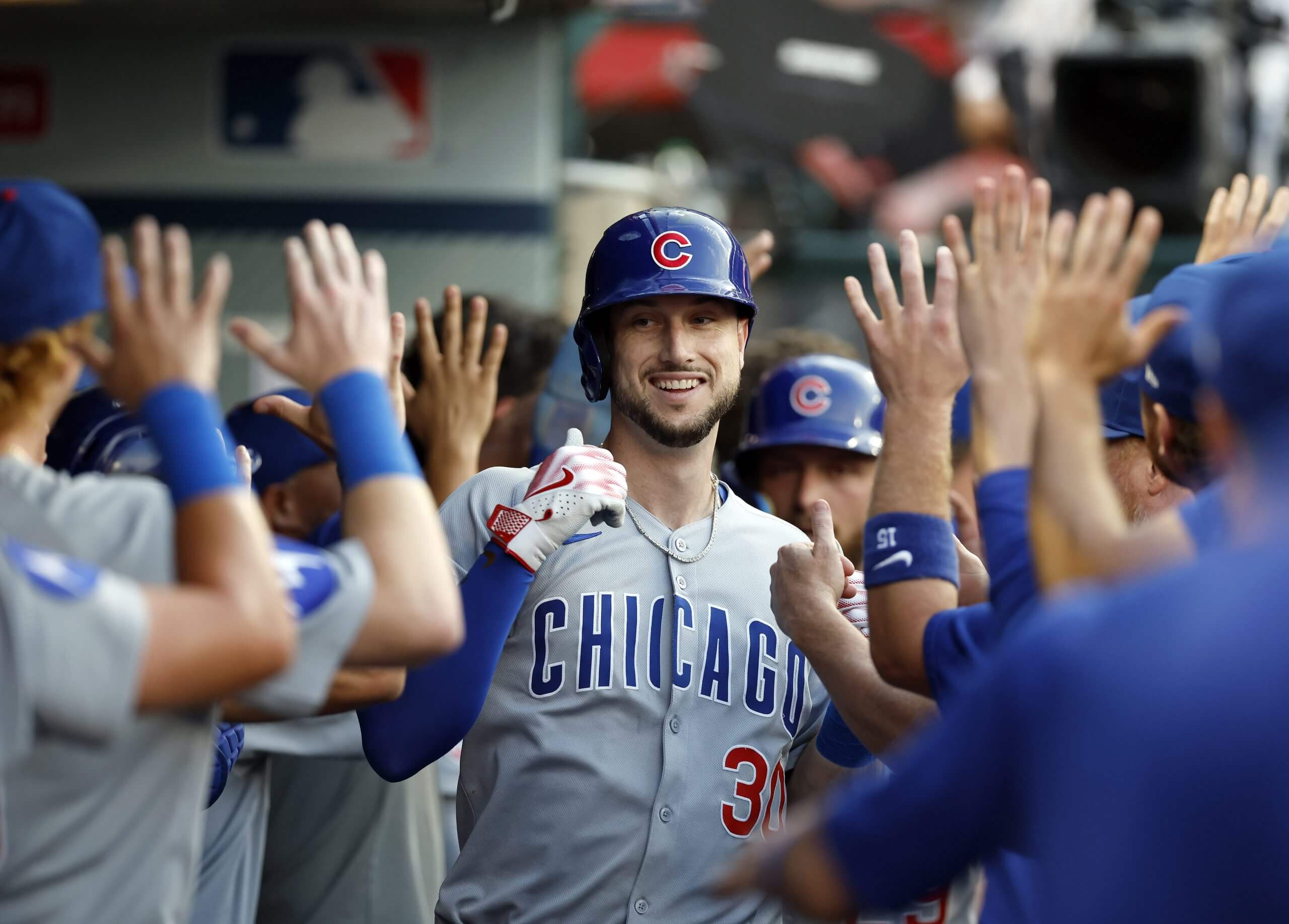 Kyle Tucker smiles in the Cubs' dugout, surrounded by several teammates waiting to congratulate him.