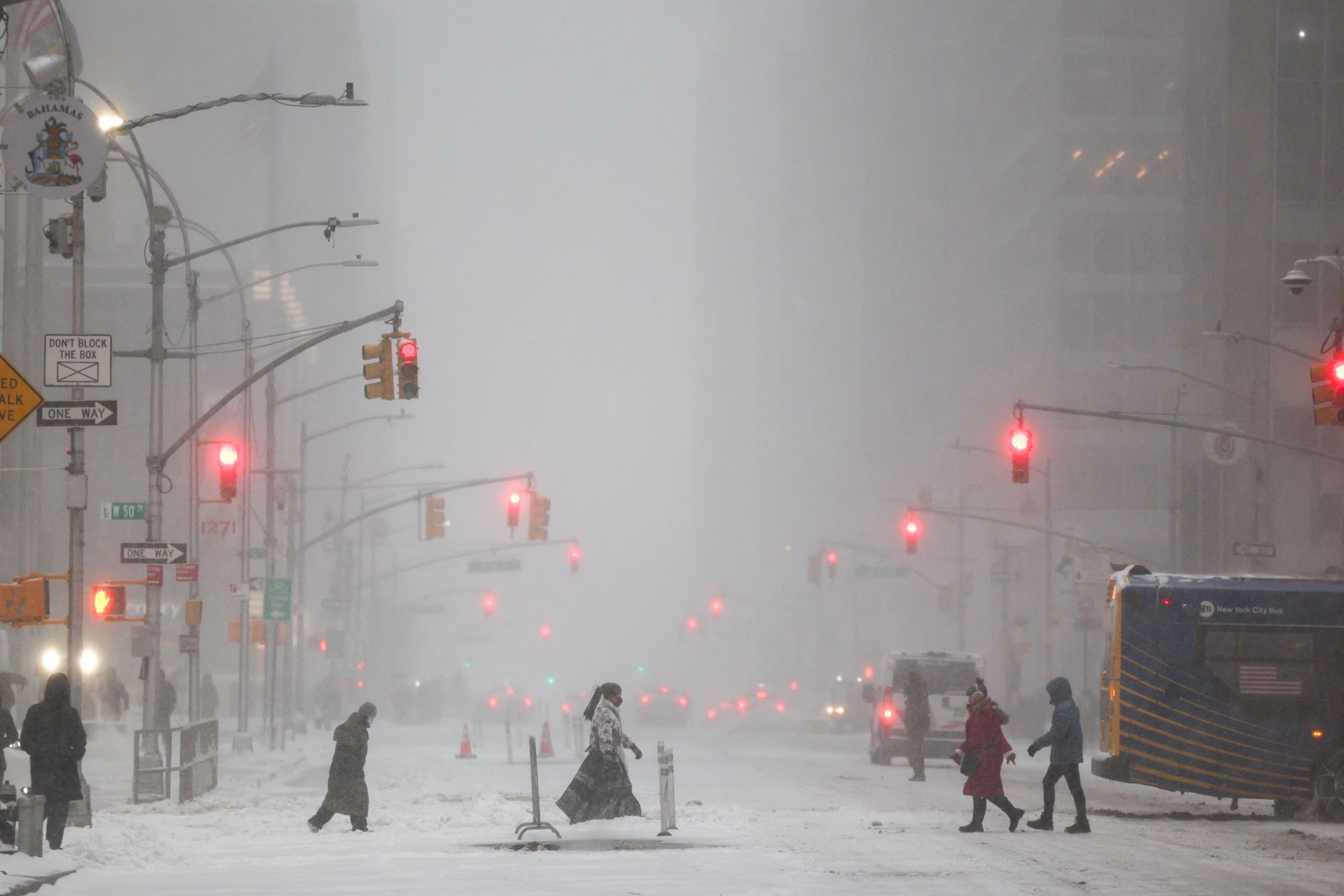 People walk across Sixth Avenue as snow falls in the Manhattan borough of New York City on January 25, 2026.