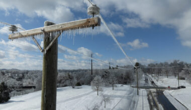Utility lines with ice stretch over a snowy scene with a plowed road.