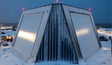 A trapezoidal building with slanted straight sides is covered in snow amidst a snowy landscape.