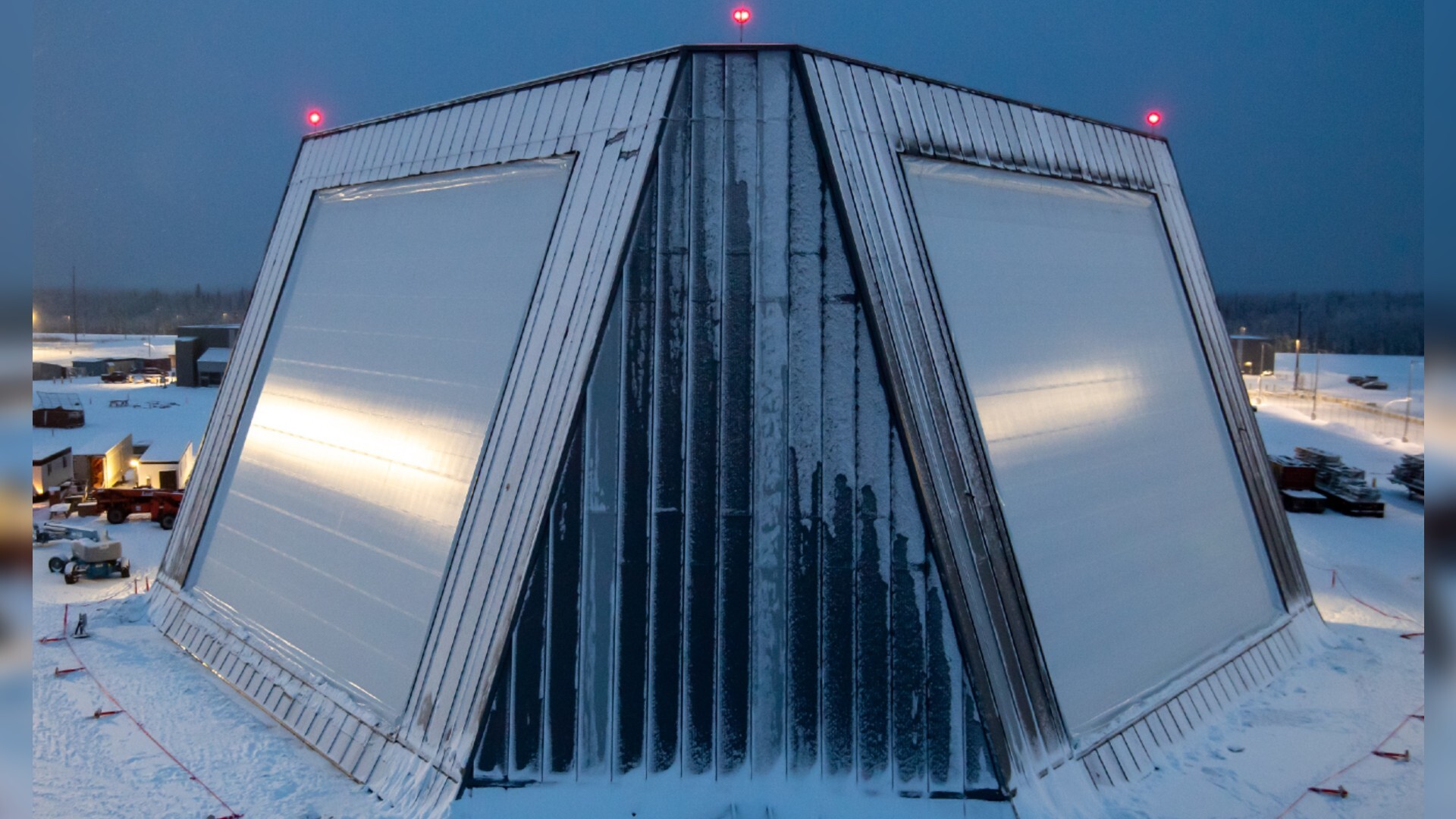 A trapezoidal building with slanted straight sides is covered in snow amidst a snowy landscape.