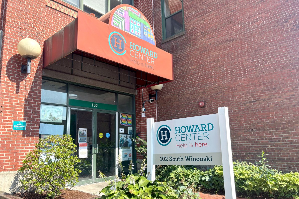 Entrance of Howard Center at 102 South Winooski, with a red awning, white sign, and surrounding plants in front of a brick building.