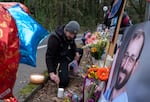 William Joyce, a nurse, adjusts a candle at a gathering outside of the Portland Veterans Affairs Medical Center on Jan. 27, 2026, in remembrance of Alex Pretti, depicted at right, a VA nurse and U.S. citizen who was killed by two U.S. Customs and Border Protection agents in Minneapolis on Jan. 24, 2026.