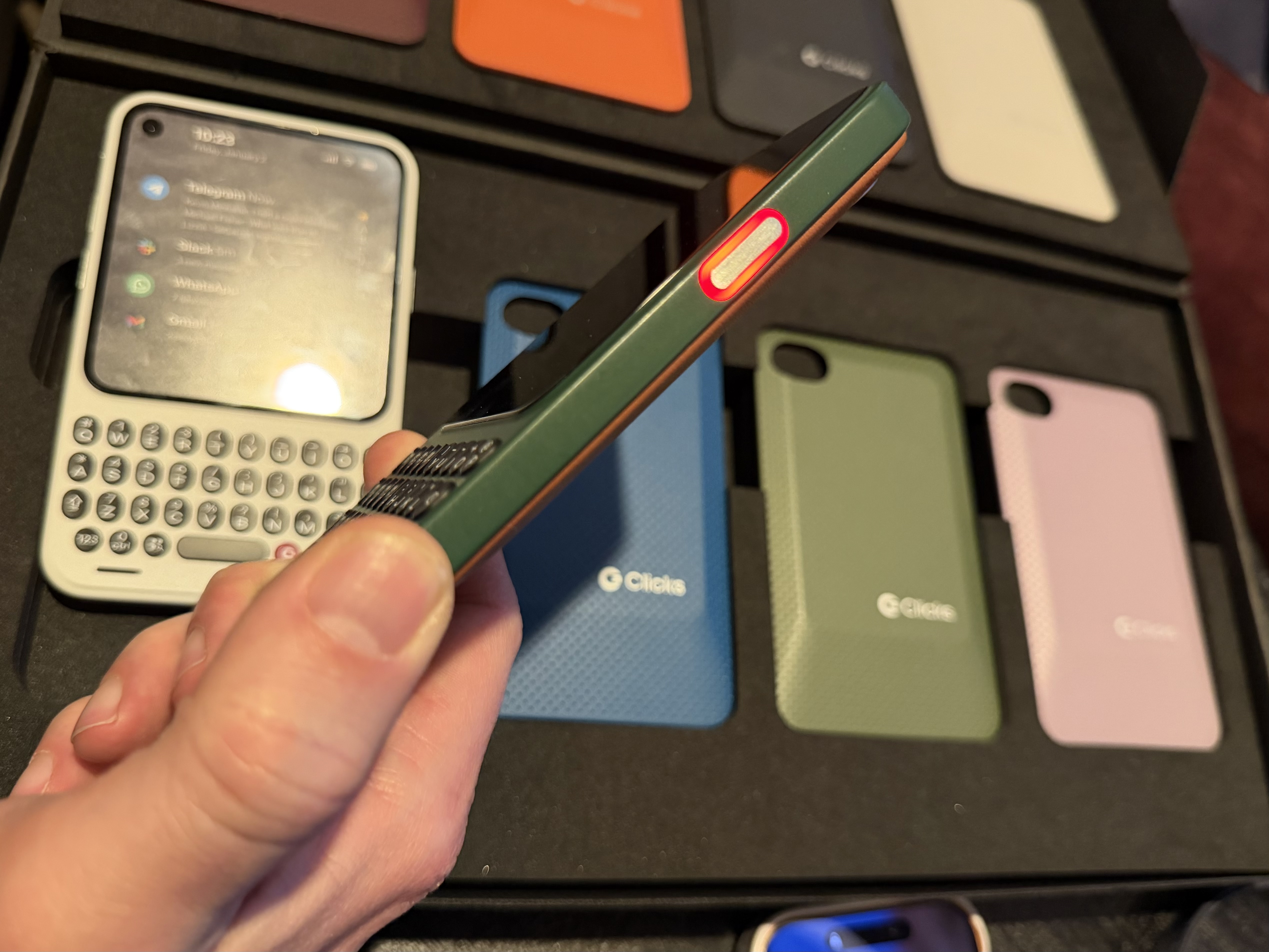 a photo showing TechCrunch holding a green Clicks Communicator device, featuring its red lit-up notification button on the side of the device.
