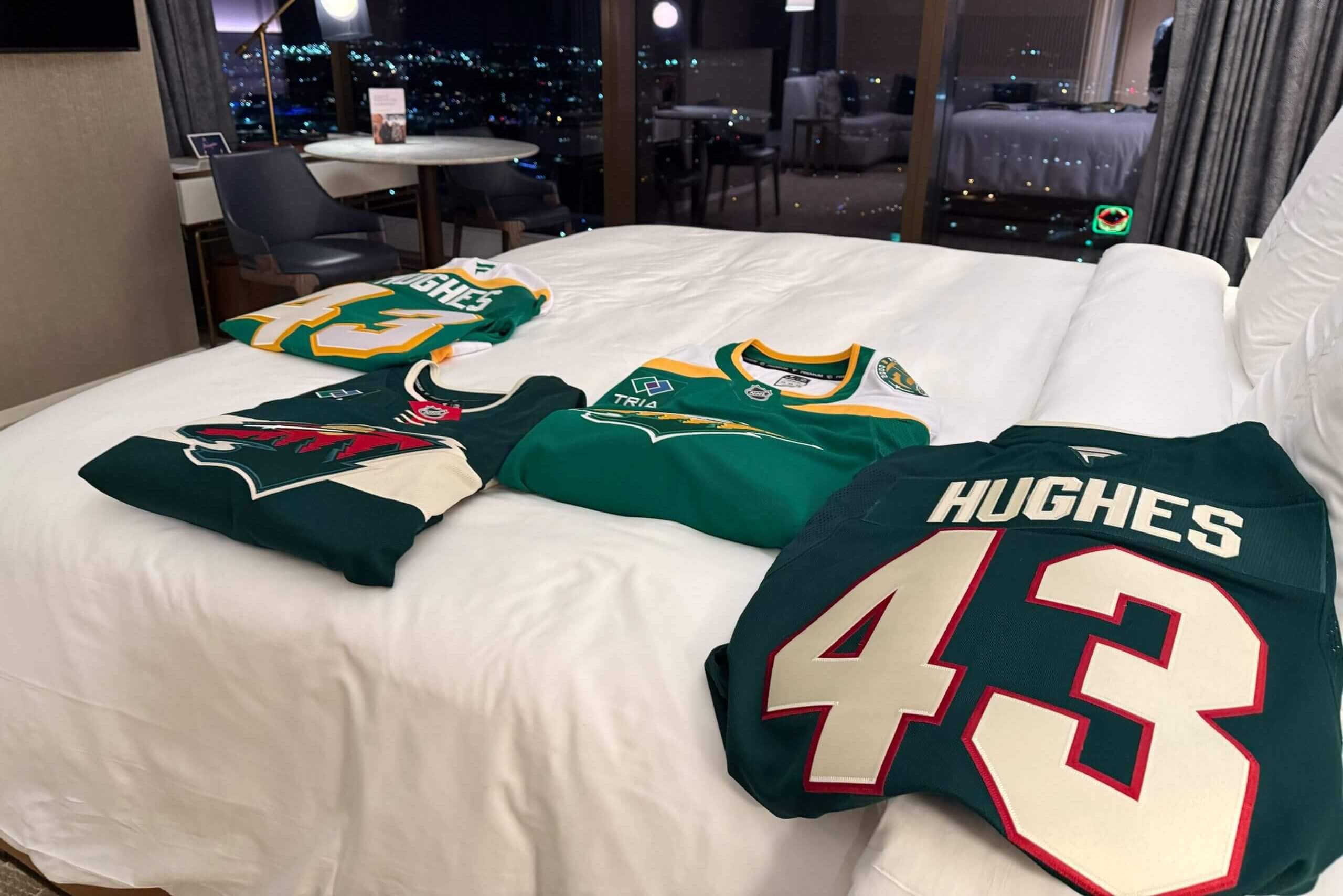 Two sets of Quinn Hughes Wild jerseys on a hotel bed.