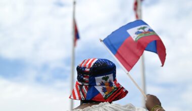 A person waves a Haitian flag while wearing a hat with both U.S. and Haitian colors at a Haitian flag festival at Somerville City Hall, on May 17, 2025.