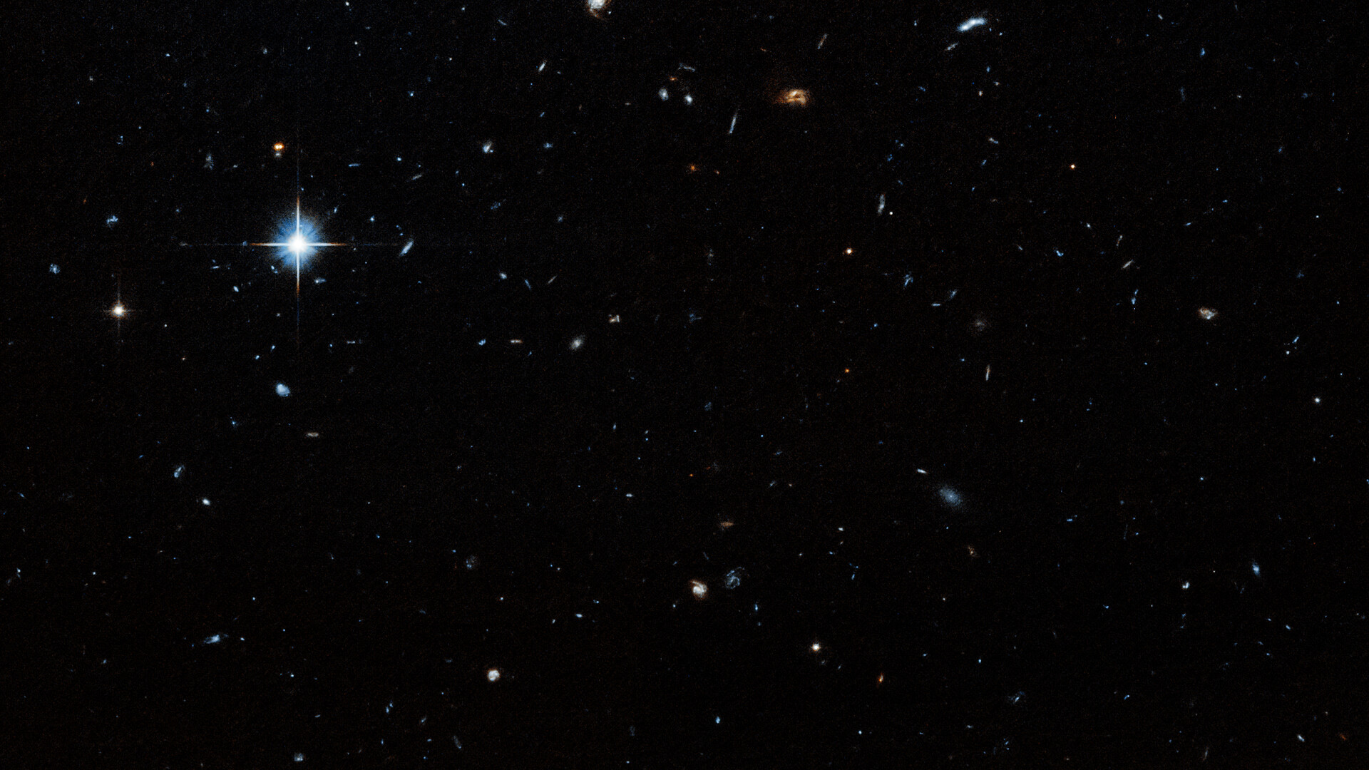 A dark field with stars and galaxies of various sizes speckled throughout the image. A particularly bright star is visible in the upper left region of the image.