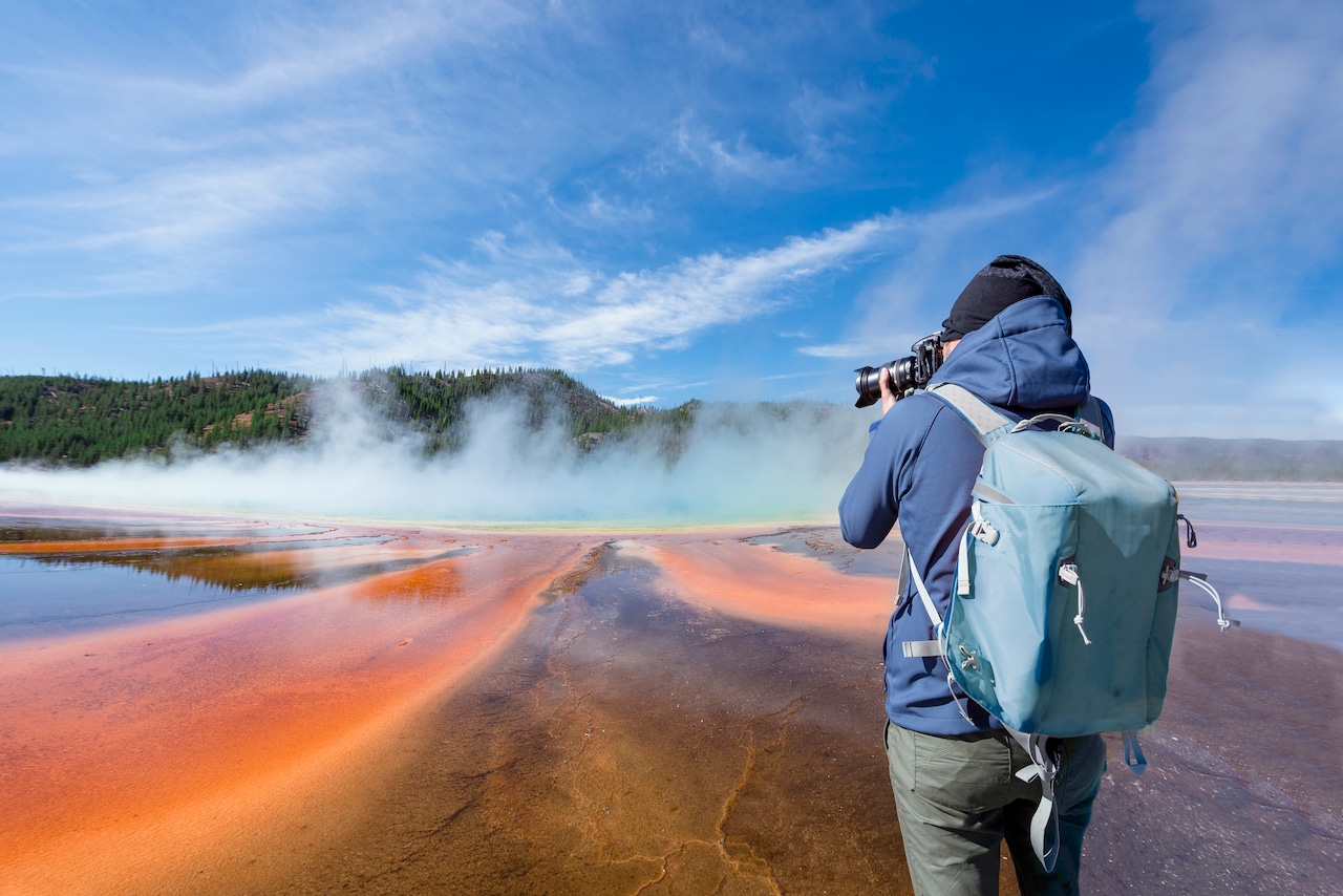 Photographer on Grand Prismatic Spring with puffy clouds overhead in Yellowstone National Park, Wyoming.