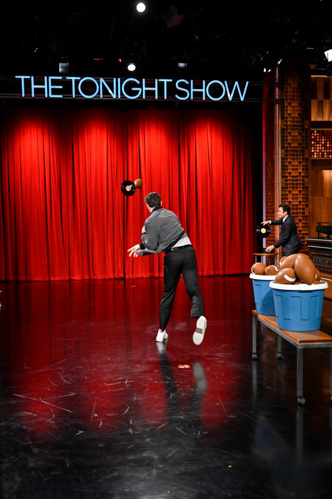 Jimmy Fallon and a guest play a game of throwing records and footballs on the Tonight Show set.