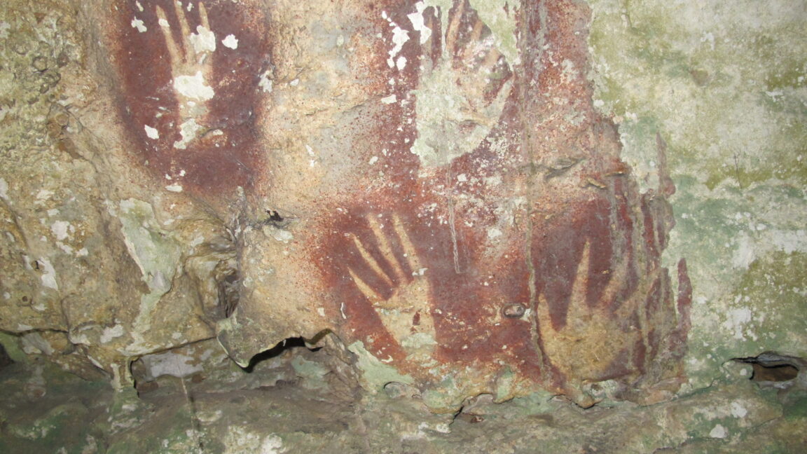 photo of pointy-fingered hand stencils on a cave wall