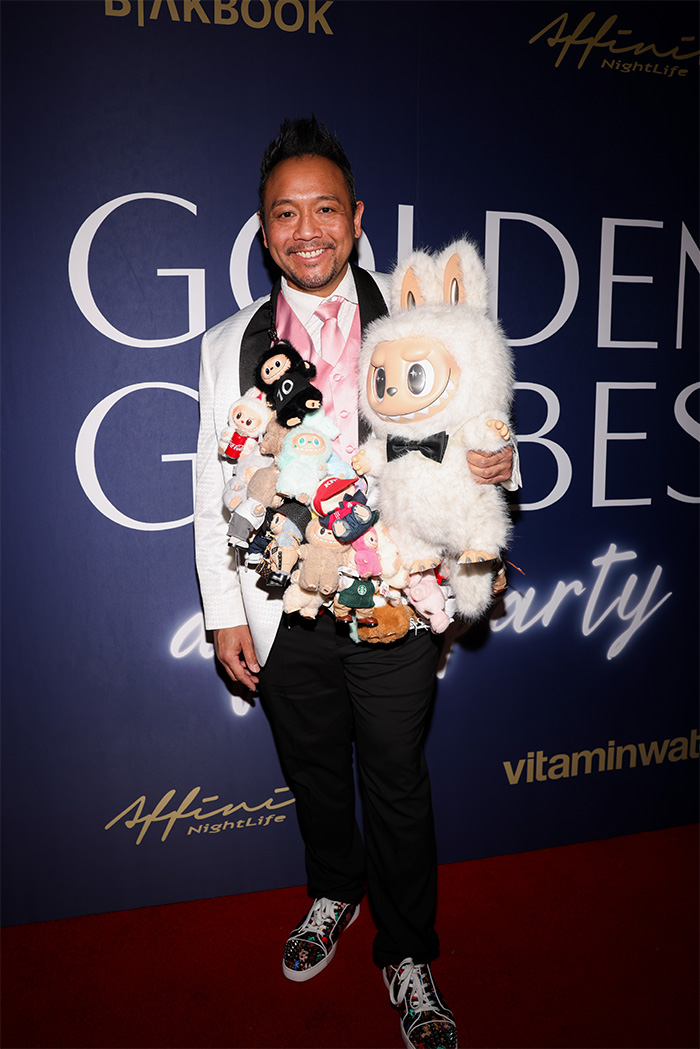 Man at 2026 Golden Globes after-party wearing a white jacket adorned with numerous stuffed toys and colorful sneakers