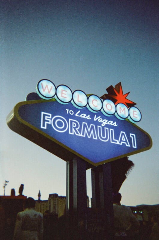 A neon sign reading "Welcome to Las Vegas Formula 1" glows at dusk, with a classic star topper and the silhouette of buildings in the background.