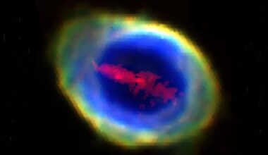 A glowing, colorful nebula with a bright yellow and green outer ring, a vivid blue center, and red cloud-like formations inside, set against a black background.
