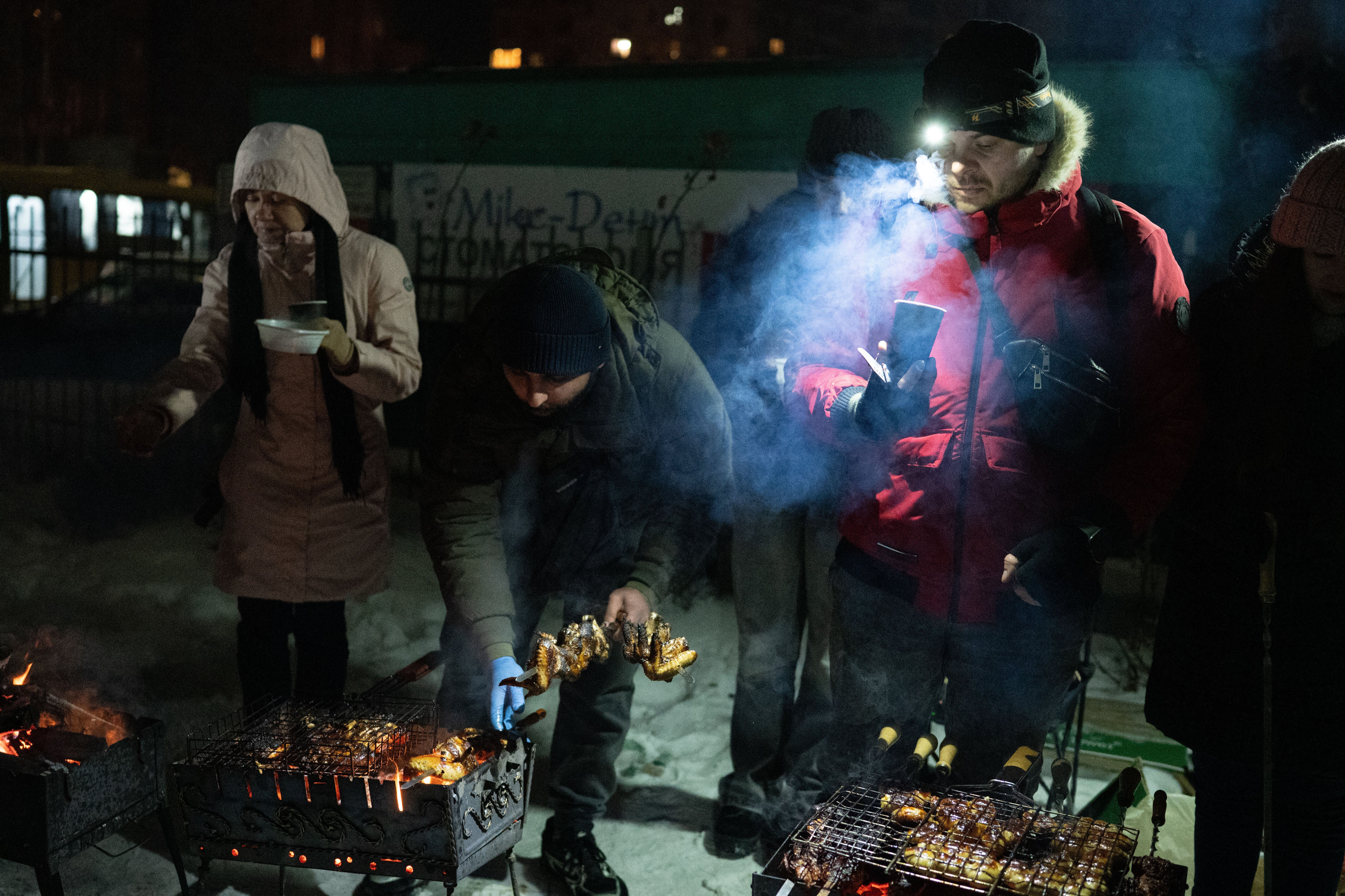 People cook on grills and warm up outside their multistory buildings during a power outage caused by Russia's regular air attacks on the country's energy sector that leave residents without power, heating and water in Kyiv