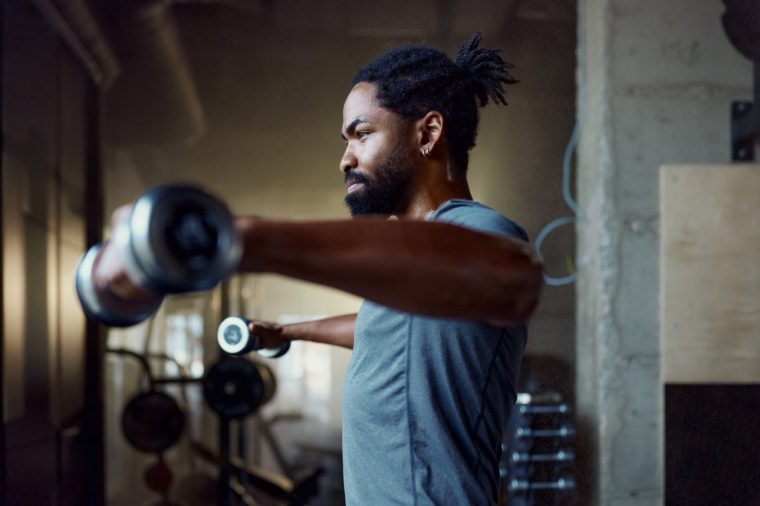 African American athletic man exercising strength during sports training with dumbbells in a health club.