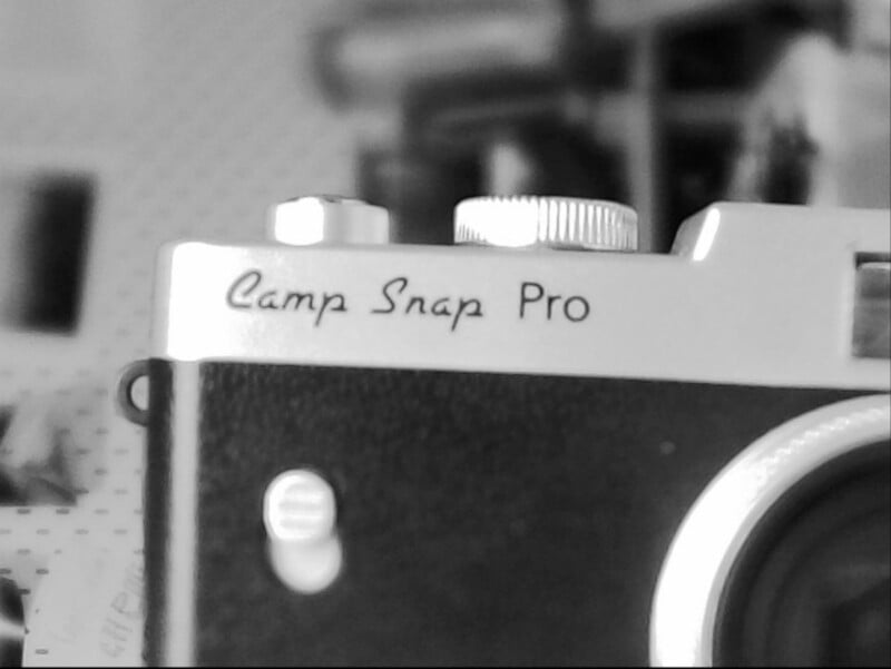 Close-up black-and-white photo of a vintage camera labeled "Camp Snap Pro" near the top, with a focus on the top control dials and part of the lens, background blurred.