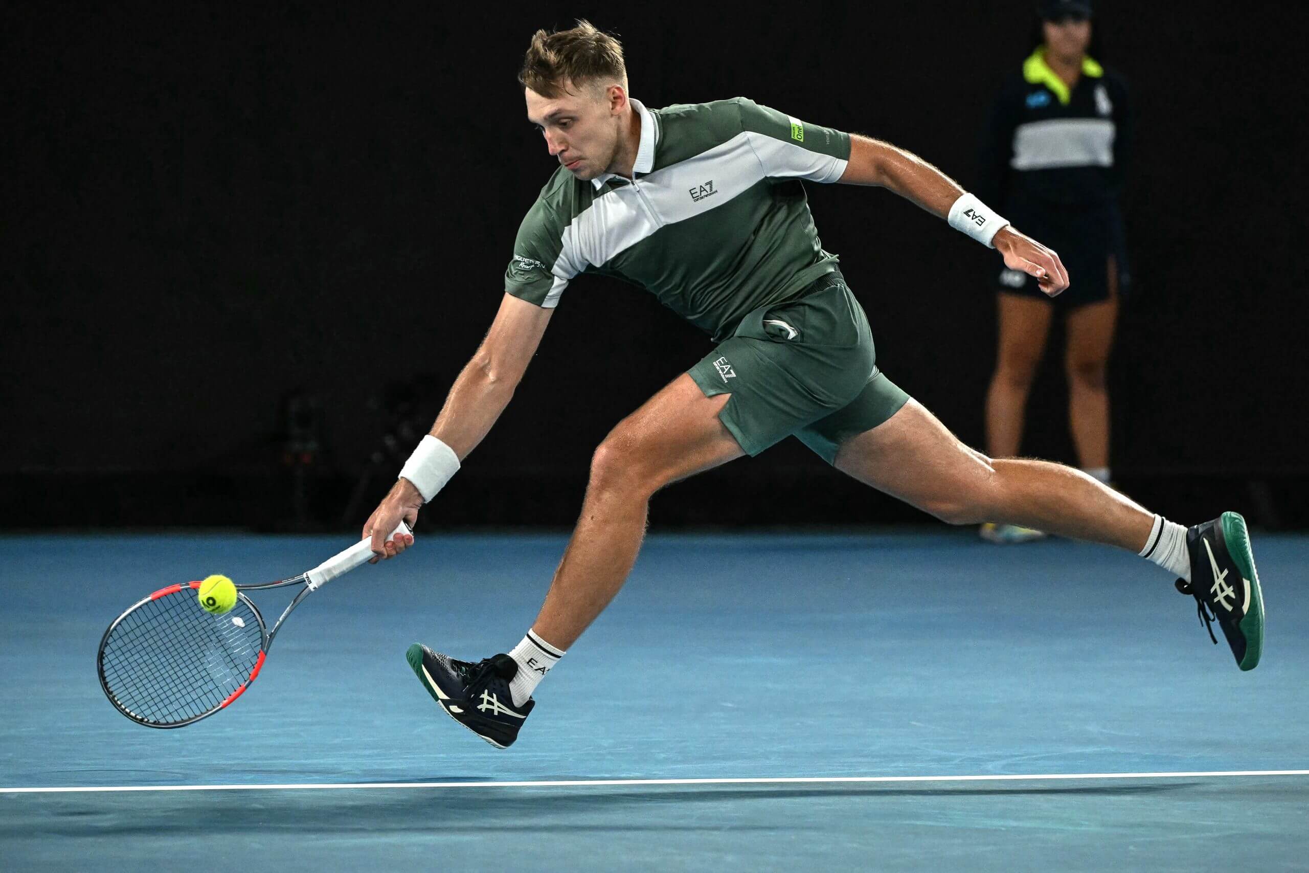 Hamad Medjedovic runs for a low forehand wearing a green and white outfit.