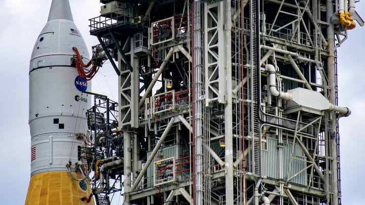 An orange rocket with a white top next to a launch tower.