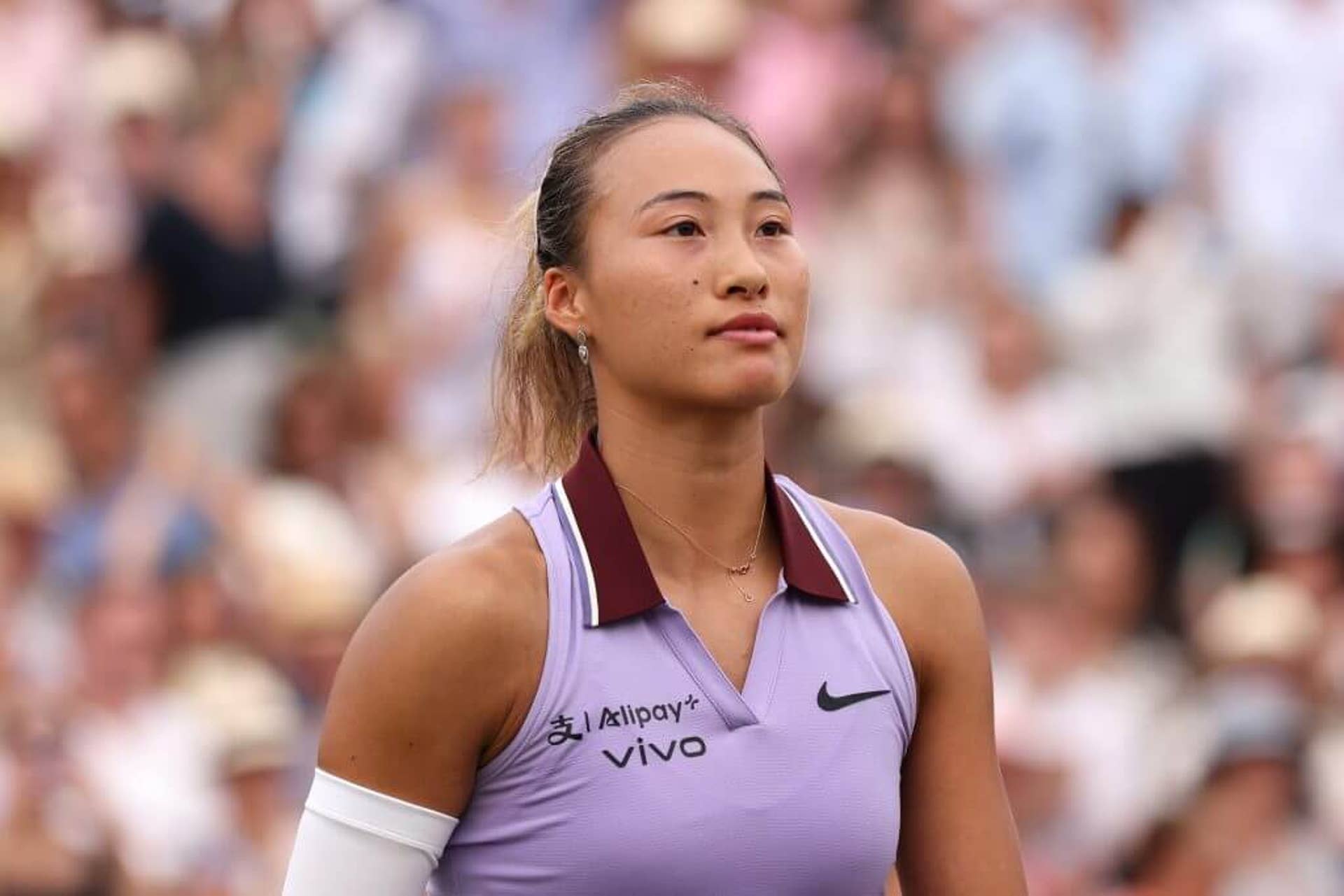Zheng Qinwen looks on with a blurred crowd behind her.
