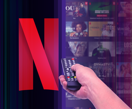 A hand holding a remote control pointed at the Netflix logo, with several shows blurred in the background