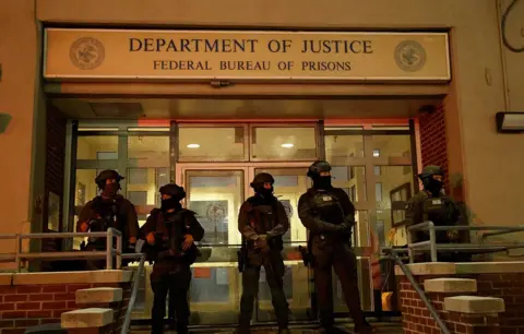 AFP via Getty Images Armed officers stand in front of Department of Justice detention center