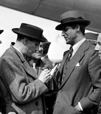 Group of men in suits and hats converse near a TWA airplane, reflecting a mid-20th-century aviation scene